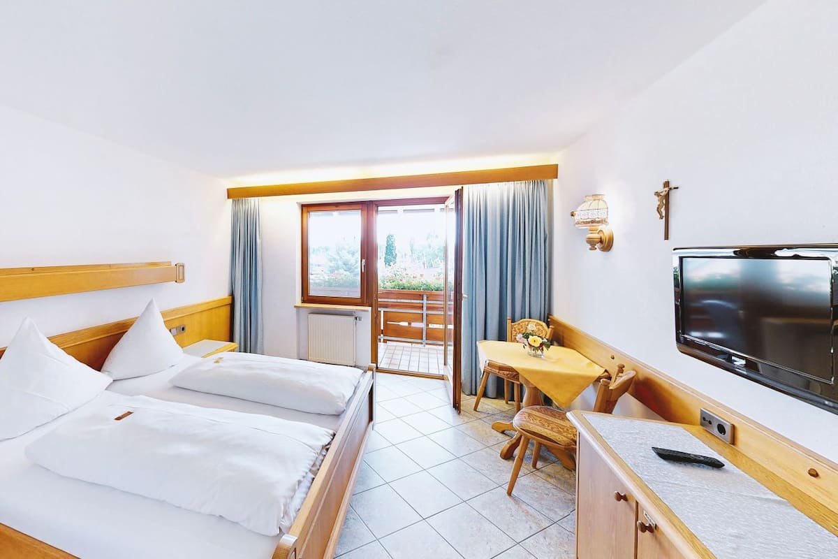 A hotel room with a bed, a desk, a TV, and a balcony with curtains.