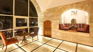 Un vestíbulo espacioso con chimenea de piedra, una zona de estar con cojines estampados y un amplio ventanal de arco.
