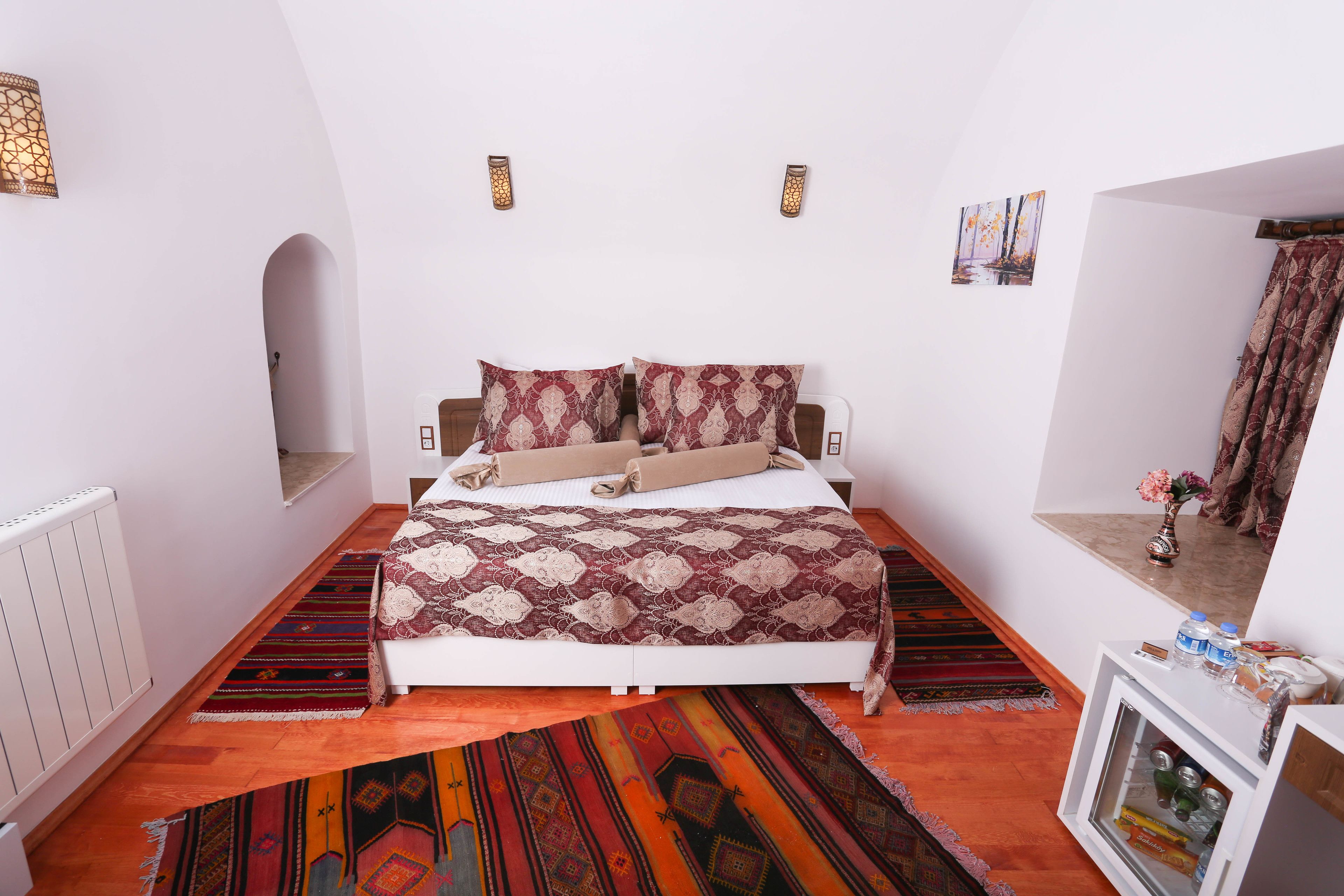 A bedroom with a bed, two wall-mounted lights, a radiator, and a small cabinet with a mirror.