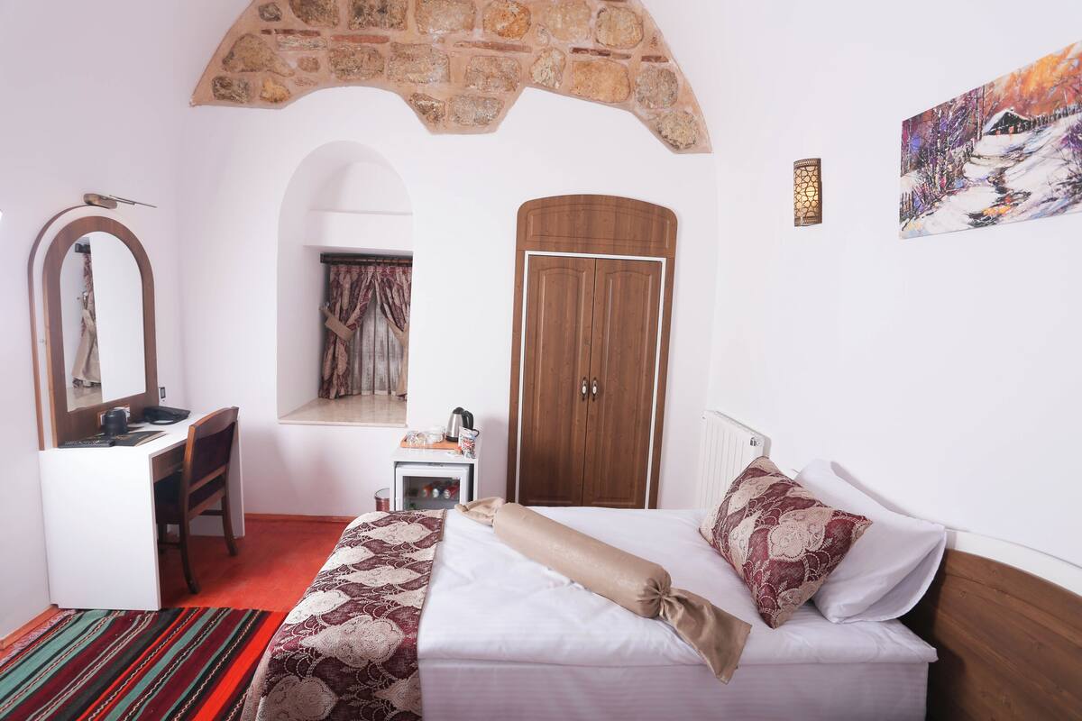 Une chambre à coucher comprenant un lit, un bureau, une chaise, une armoire, une arche en pierre et un tableau.