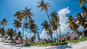 A beach with palm trees and thatched-roof huts. - Savera Beach Houses (Jambiani)