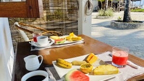 A breakfast table with a plate of fruit, two cups of coffee, and a glass of red juice. - Savera Beach Houses (Jambiani)