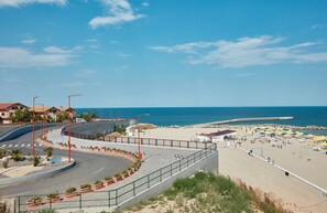A coastal road leading to a beach with a clear view of the sea, a paved walkway, and beach umbrellas. - Gabizz Apartments (Constanta)