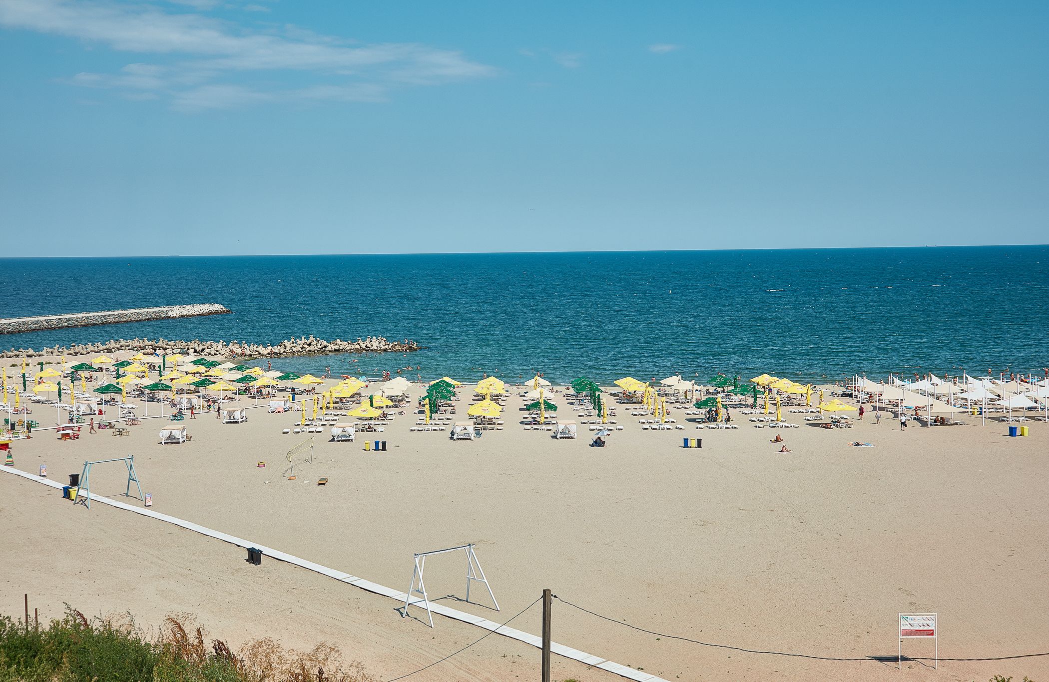 A beach with umbrellas and sun loungers, a pier, and a clear blue sky.