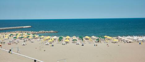 A beach with umbrellas and sun loungers, a pier, and a clear blue sky.