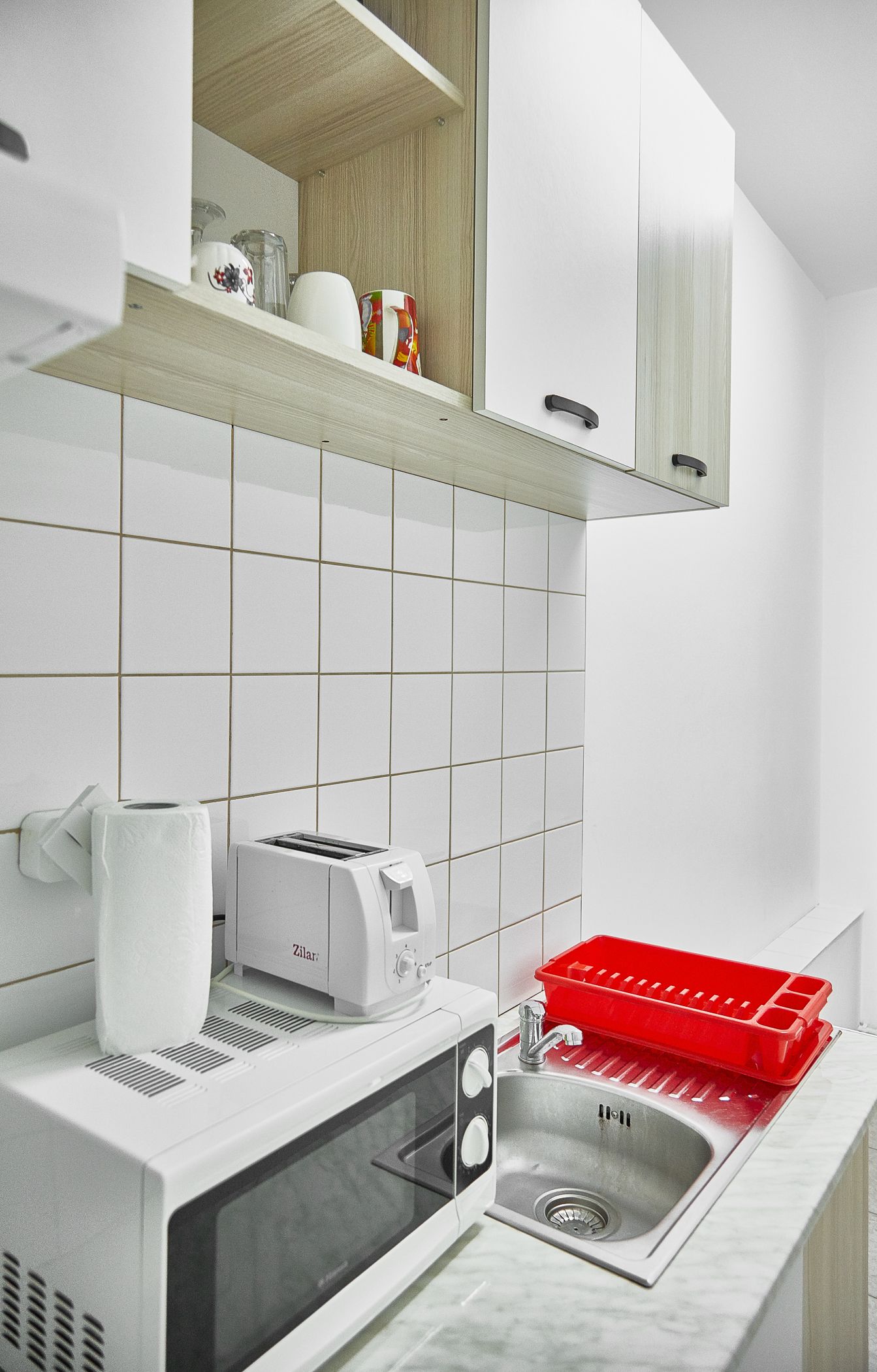 A modern kitchen with white tiles, a built-in oven, a toaster, and a red dish rack.