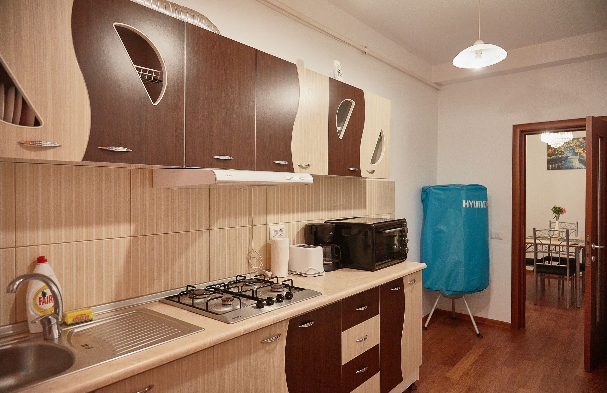 Une cuisine moderne avec des meubles en bois, une cuisinière à gaz, une machine à café et un sac à linge bleu.