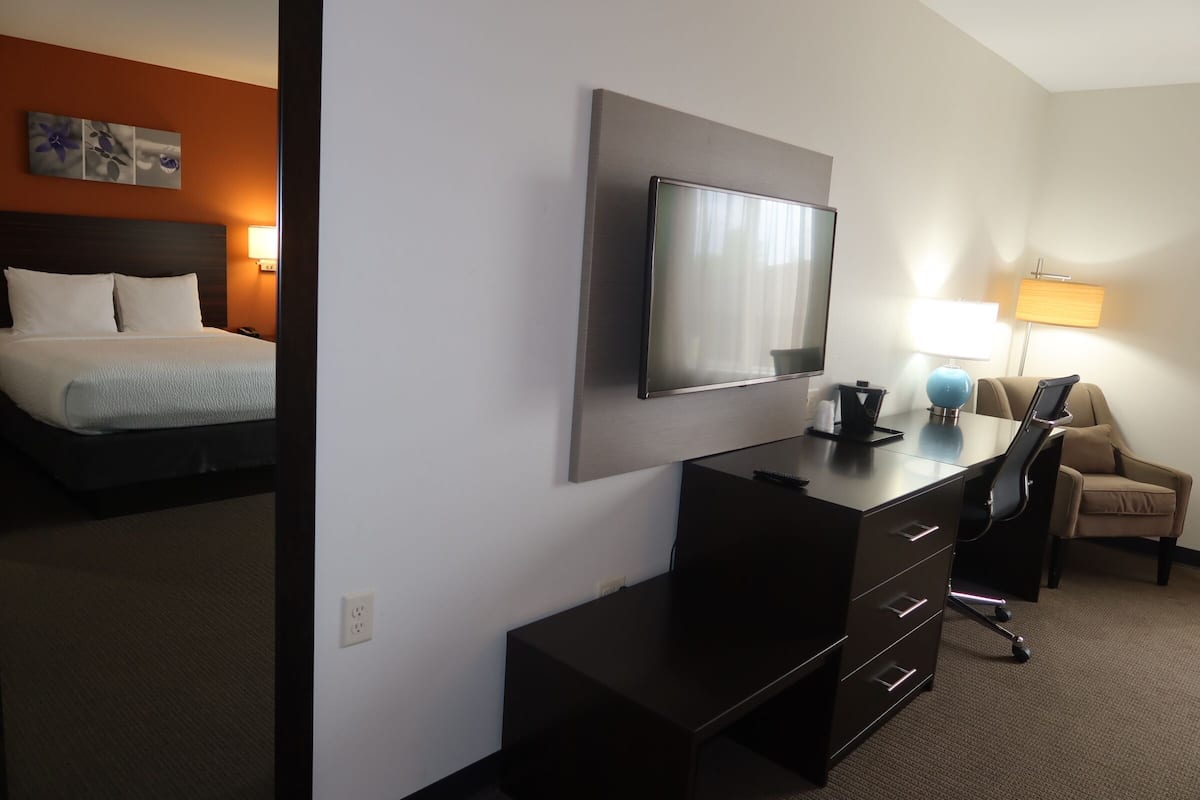 Quarto de hotel com cama, escrivaninha, televisão de tela plana, uma cadeira e abajur.