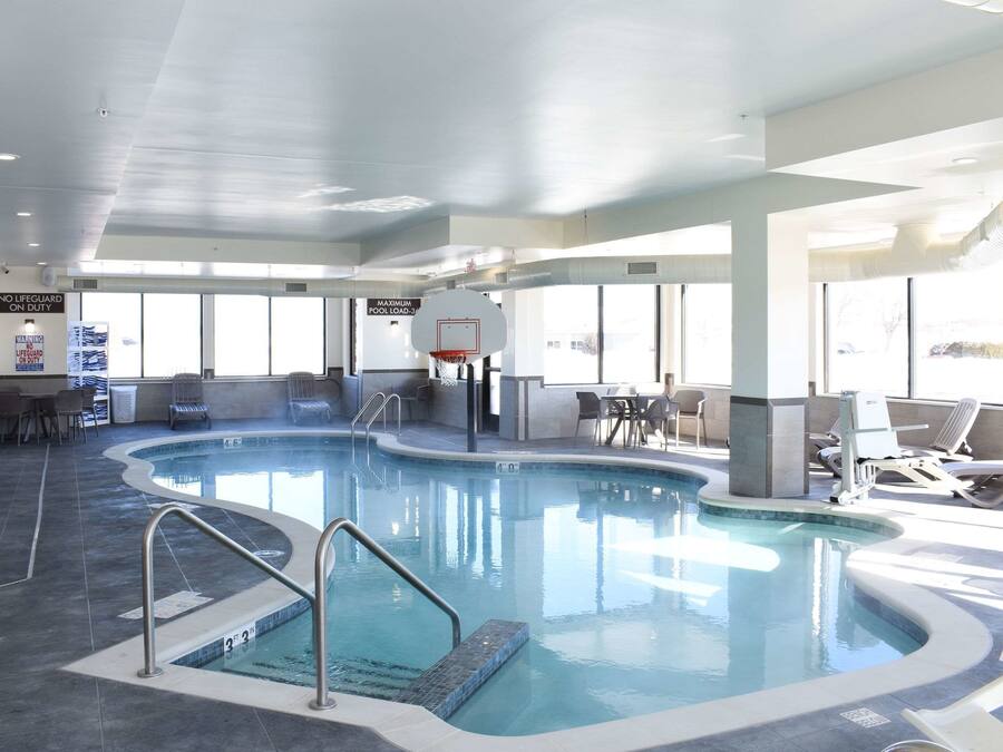 Une piscine intérieure équipée d’un panier de basketball, de chaises longues et d’un espace détente avec des tables.
