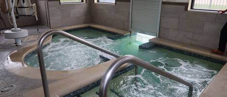 A spa pool with a metal railing, a notice sign, and a window with blinds.