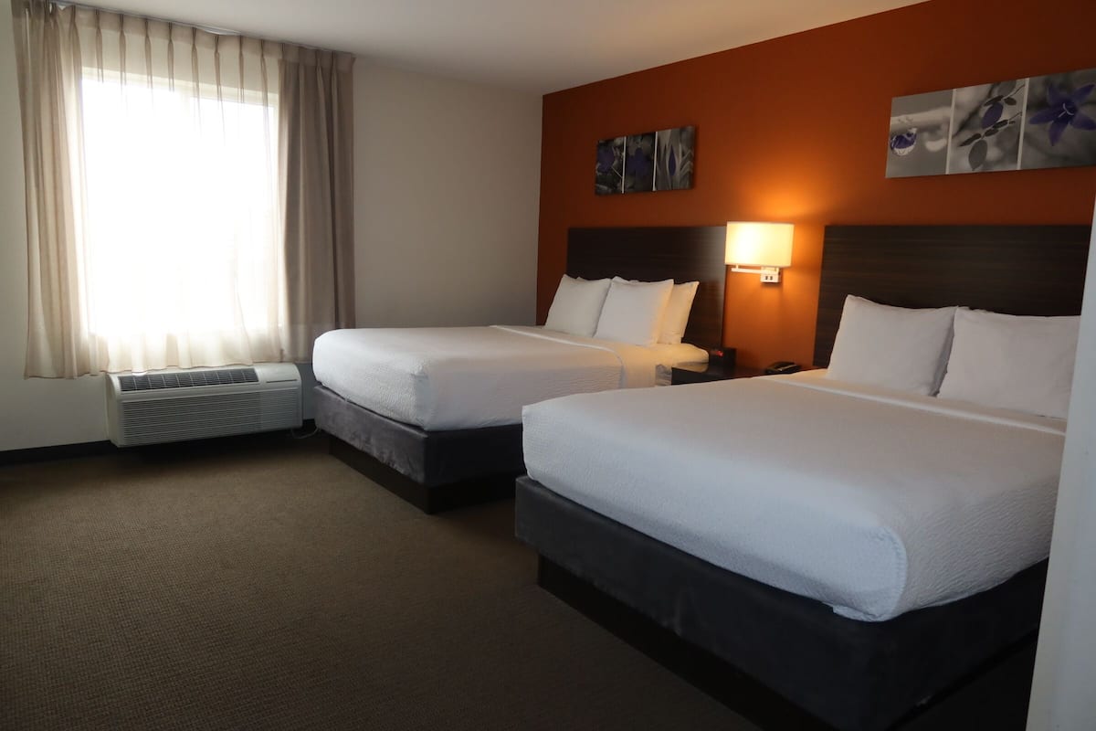Quarto de hotel com duas camas, uma luminária fixada na parede e uma janela grande com cortinas.