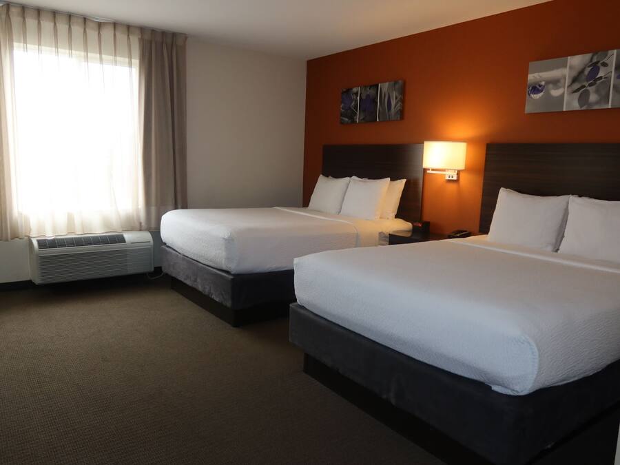 A hotel room with two beds, a wall-mounted lamp, and a large window with curtains.