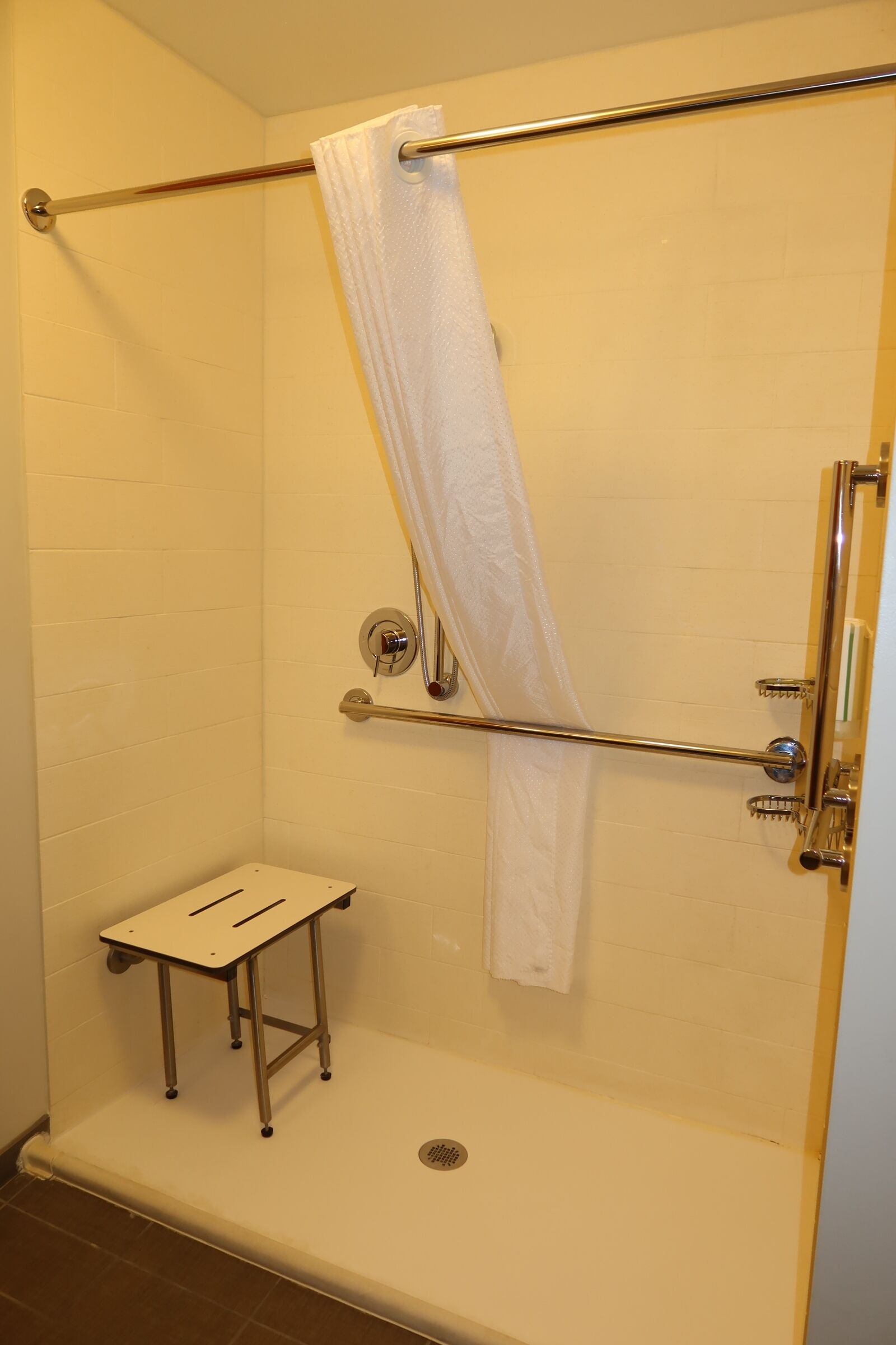 A shower with a white towel, a metal grab bar, and a small stool.