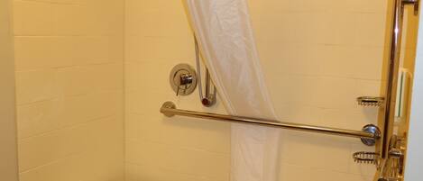 A shower with a white towel, a metal grab bar, and a small stool.