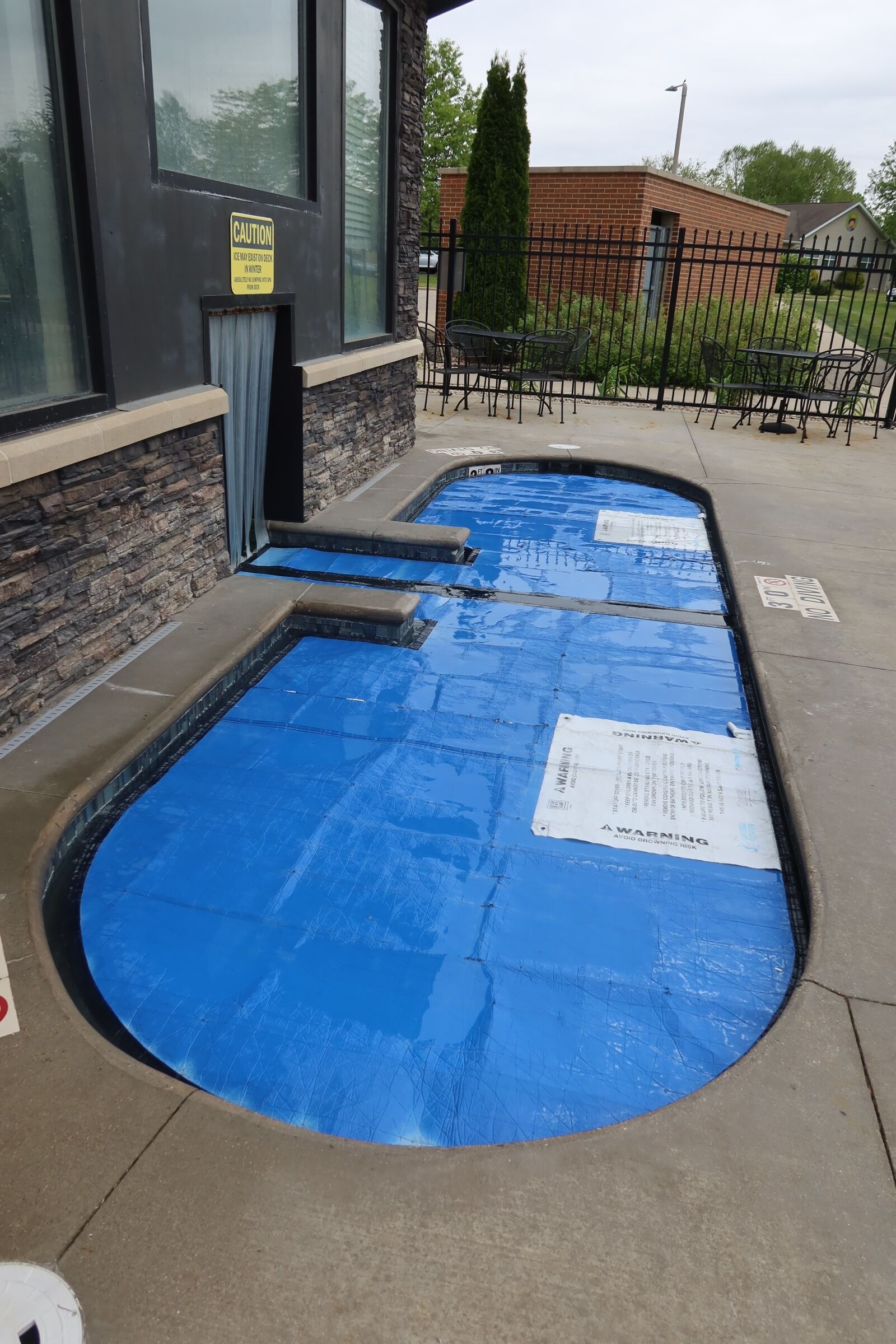 A pool with caution tape, a building with large windows, and a fenced area with outdoor seating.