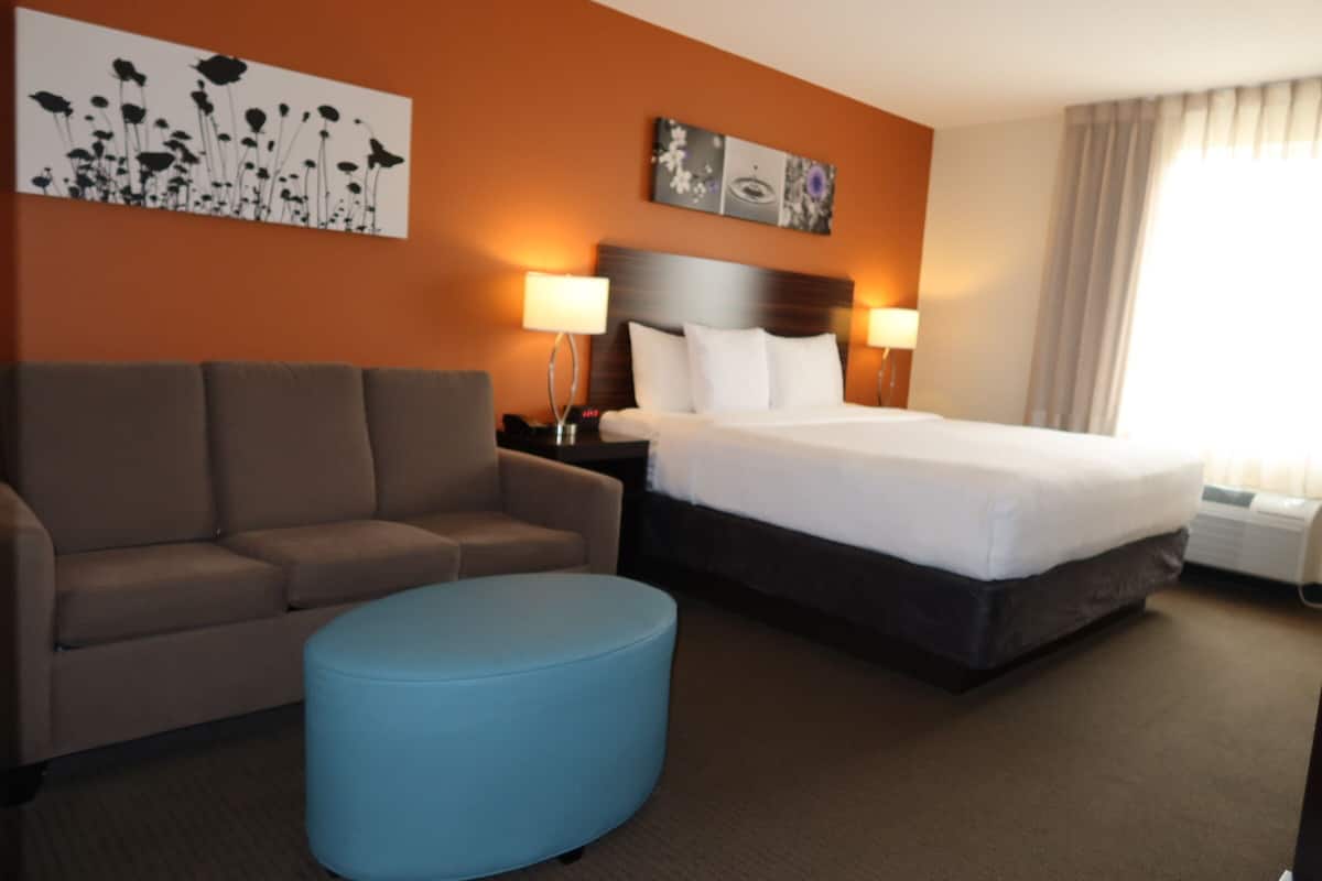 Quarto de hotel com cama, sofá, banquinho azul, mesa de cabeceira e decoração na parede.
