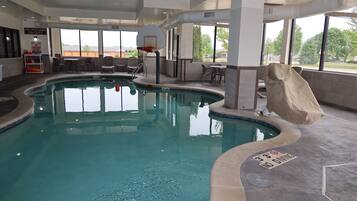 An indoor swimming pool with a no diving sign, a basketball hoop, and a covered seating area.