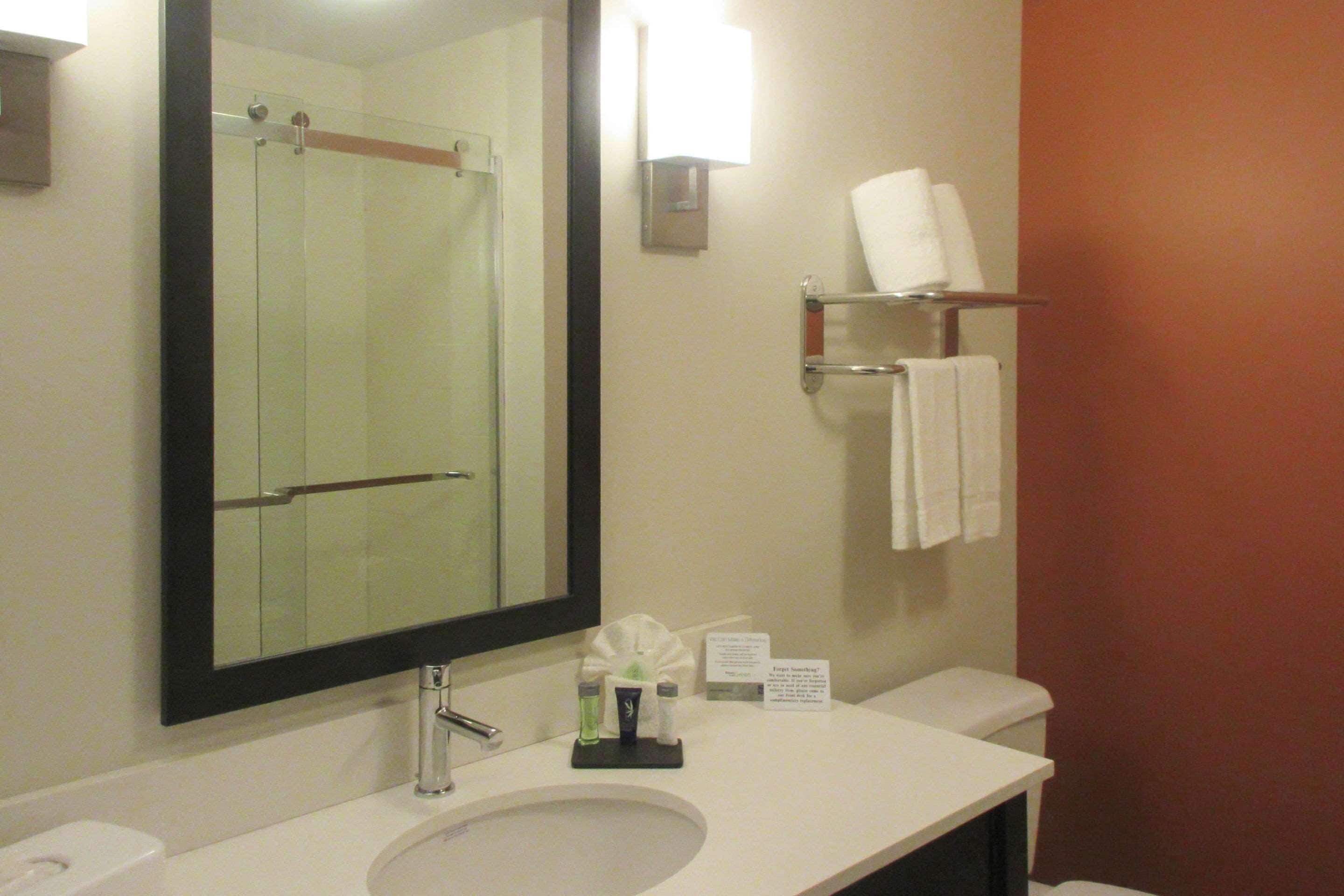 Un bagno d'hotel con lavandino, specchio, asciugamano e un cartello con informazioni.