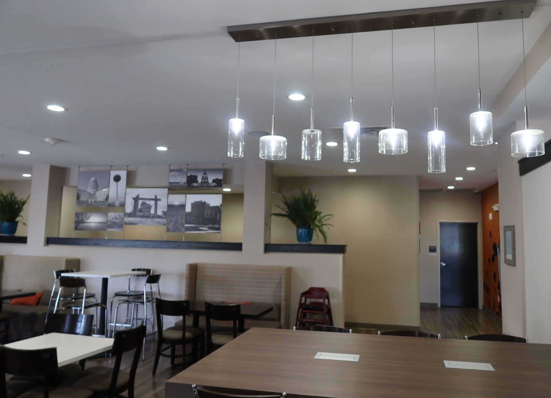 Un moderno vestíbulo de hotel con zona de comedor, iluminación colgante y una obra de arte con vistas a la ciudad.