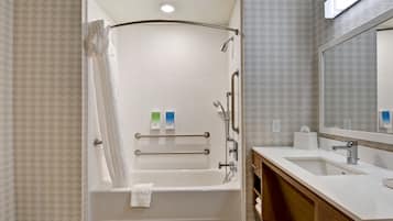 A modern bathroom with a walk-in shower, grab bars, a bathtub, a sink, and a mirror.