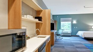 Una habitación de hotel moderna con microondas, pileta y un escritorio con silla.