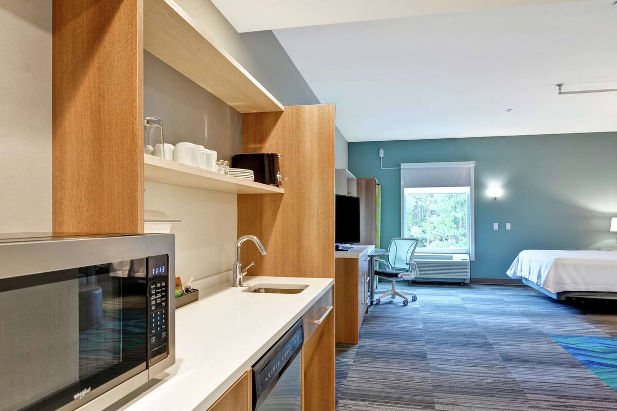Una habitación de hotel moderna con microondas, pileta y un escritorio con silla.