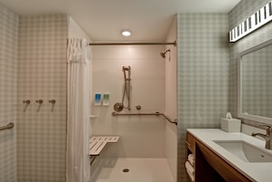 Un baño moderno con ducha, barras de apoyo, tocador con lavabo y espejo.