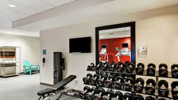 A gym with a bench, a wall-mounted TV, and a rack of dumbbells.