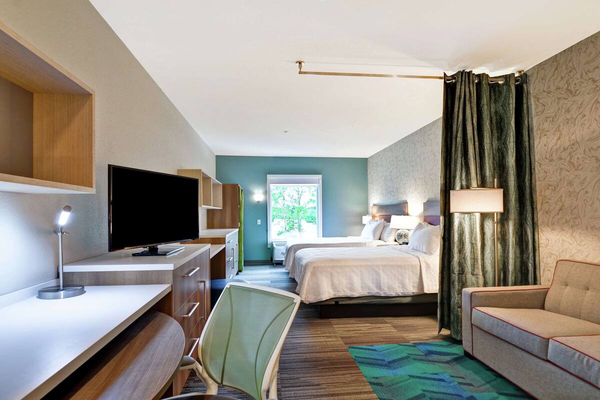 Habitación de hotel con cama, escritorio con computadora, una silla, un sofá y ventana con cortinas.