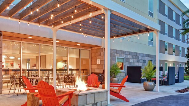 Un área de estar al aire libre con chimenea, sillas Adirondack rojas y un porche cubierto con luces colgantes.