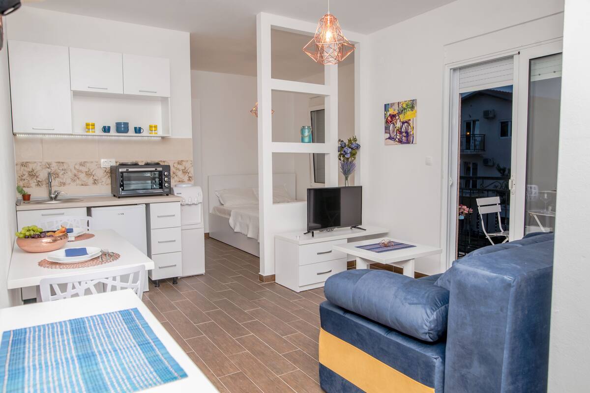 A compact living space with a kitchenette, a dining area, a sofa, and a TV.
