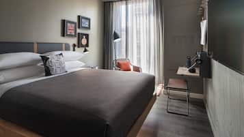 A modern hotel room with a large bed, a desk with a chair, a flat-screen TV, and a window with curtains.
