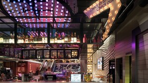 A multi-level bar area with a check-in/out sign, a staircase, and a variety of bottles displayed on shelves. - Moxy San Diego Downtown/Gaslamp Quarter (San Diego)