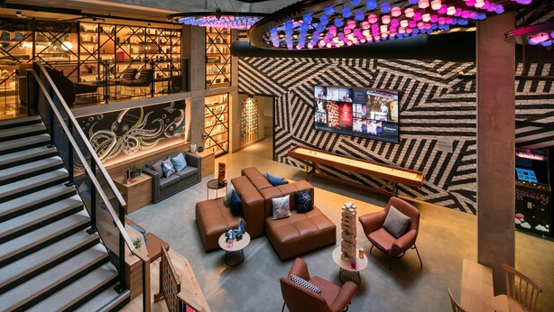 A modern lounge area with a staircase, seating arrangements, and a bar area with a patterned wall and hanging lights. - Moxy San Diego Downtown/Gaslamp Quarter (San Diego)