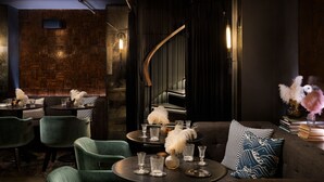 A dimly lit bar area with a brick wall, a curved staircase, and a seating area with a sofa and chairs. - Moxy San Diego Downtown/Gaslamp Quarter (San Diego)