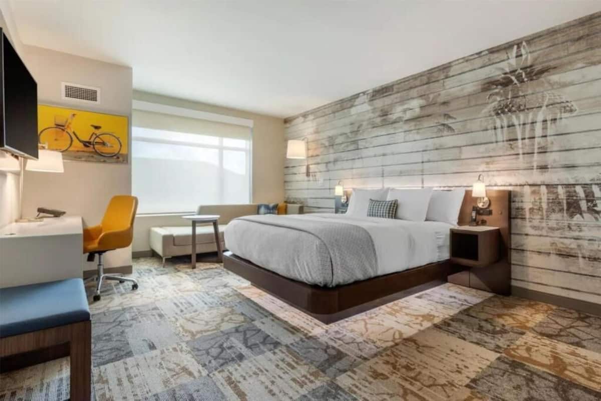 A modern hotel room with a large bed, a desk, a chair, and a television.