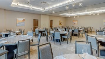 A spacious conference room with multiple tables set for dining, featuring modern chairs and a contemporary chandelier.