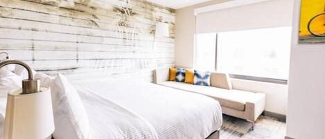 Un dormitorio moderno con cabecera de madera, una cama grande con ropa blanca, una mesita de noche con lámparas y una ventana con vistas.