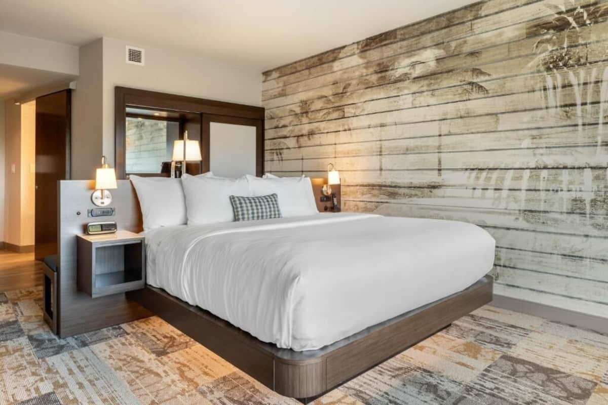 A modern hotel room with a large bed, bedside lamps, a nightstand, and a rustic wooden wall.