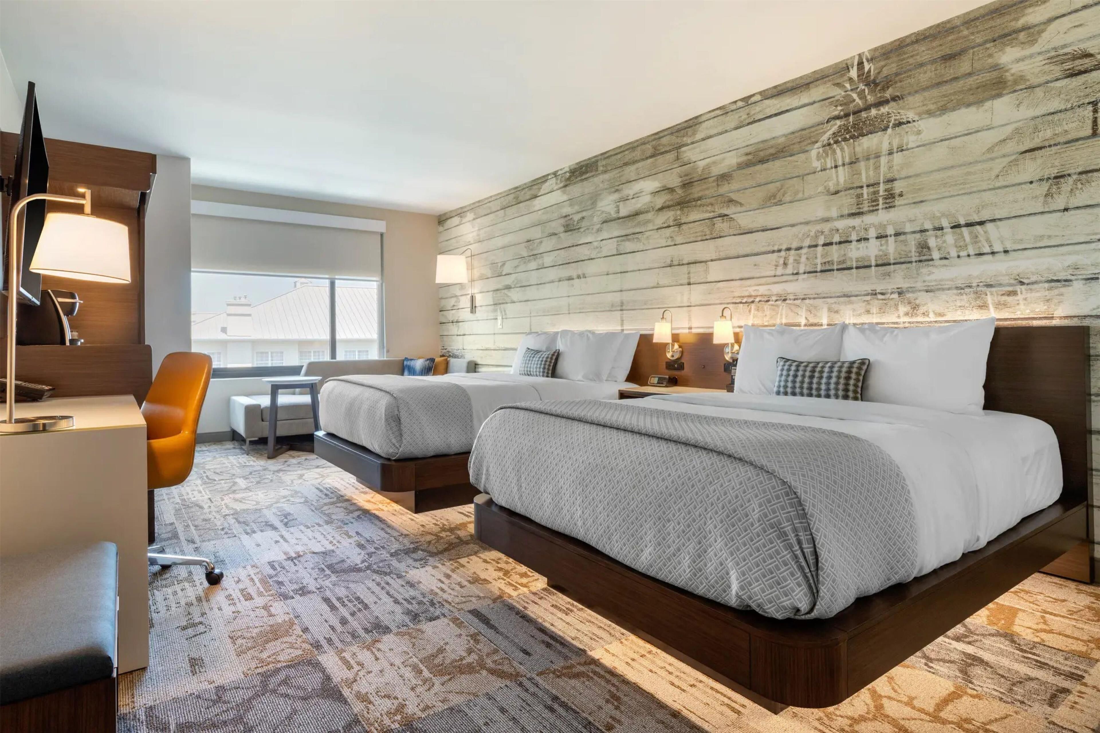 A hotel room with a large bed, a desk, a chair, and a window.