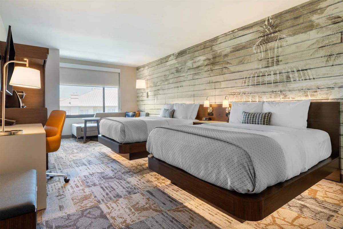 A hotel room with a large bed, a desk, a chair, and a window.