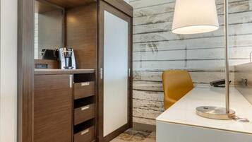 Una habitación de hotel moderna con un armario de madera, un escritorio con lámpara y una cafetera.