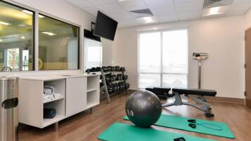 Un gimnasio con equipo de ejercicio, televisión y ventana.