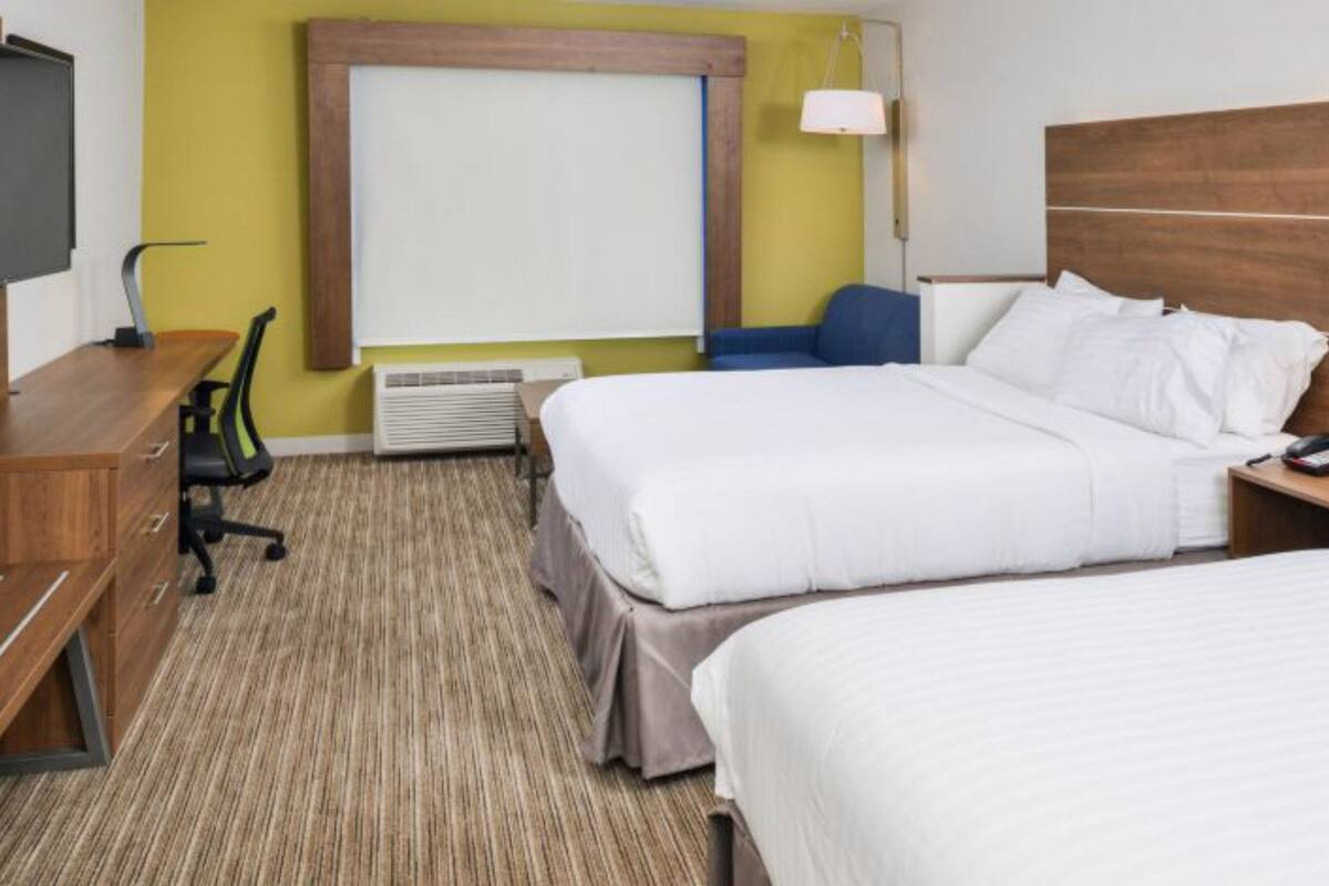 Habitación de hotel con dos camas, un escritorio, una silla, un televisor y una ventana.