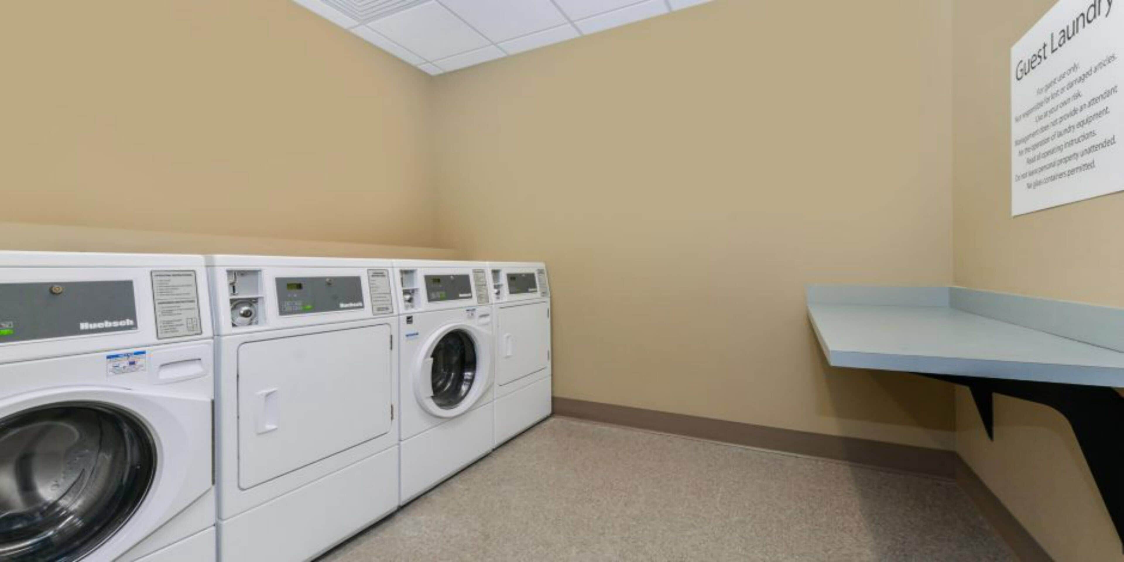 A laundry room with multiple white front-loading washing machines and a blue bench.