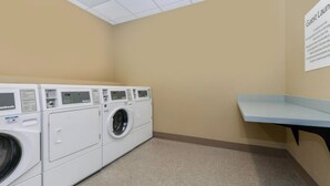A laundry room with multiple white front-loading washing machines and a blue bench. - Holiday Inn Express Alliance by IHG (Alliance)