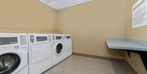 A laundry room with multiple white front-loading washing machines and a blue bench. - Holiday Inn Express Alliance by IHG (Alliance)