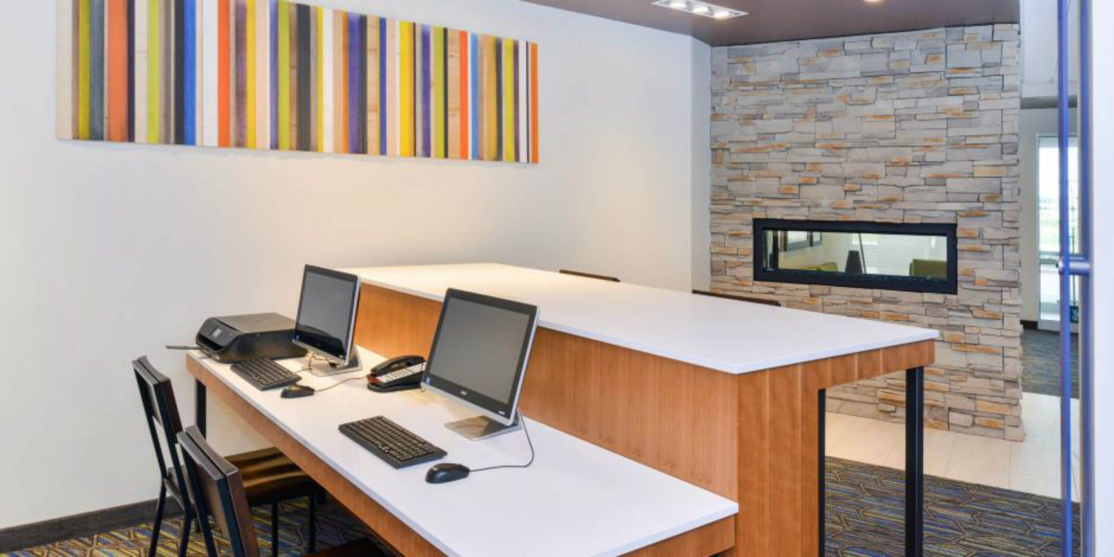 Uma sala de conferências com duas mesas, cada uma com um computador e teclado, e um grande janelão com parede de pedra.