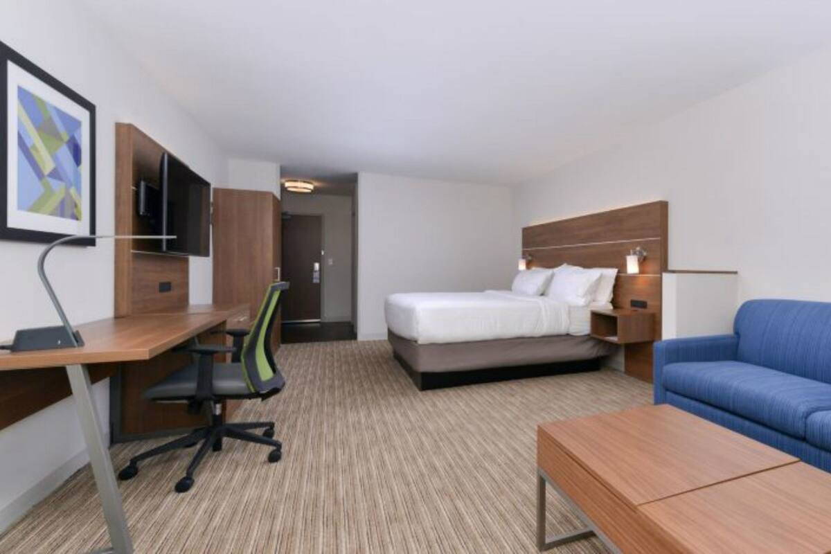 Una habitación de hotel con cama, escritorio con silla, sofá y televisor en la pared.