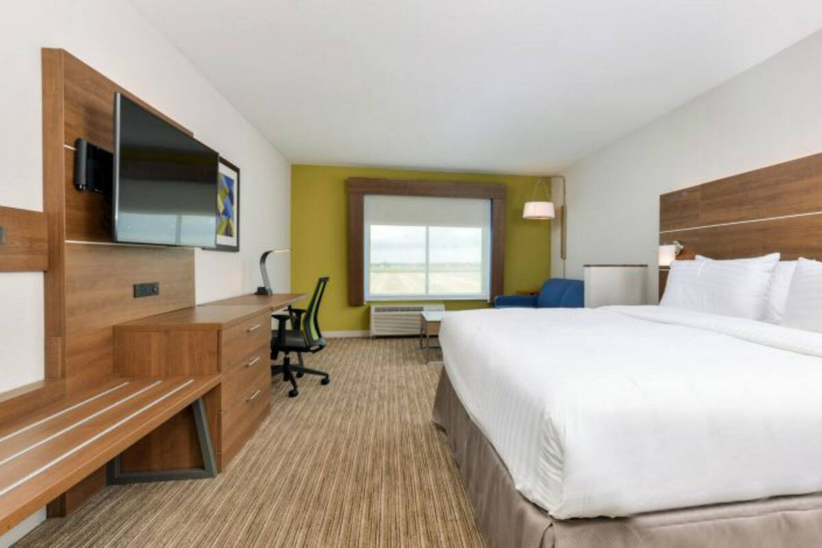 Una habitación de hotel con cama, escritorio, silla, televisor y ventana.